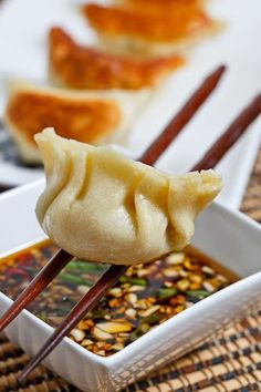 two chopsticks with food in a bowl on a table next to other foods