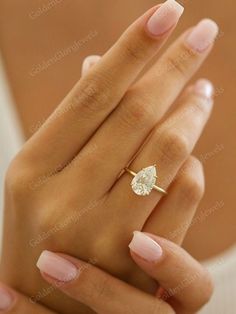 a woman's hand holding a ring with a diamond on it and pink nails