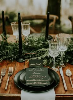 the table is set with black plates and silverware, greenery on each plate