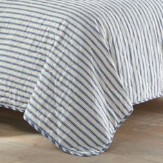 a blue and white striped comforter on top of a wooden floor next to a bed