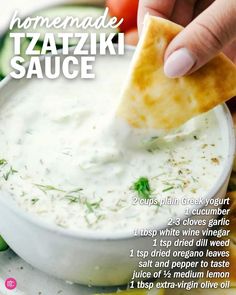 a hand dipping a tortilla chip into a bowl of tzatziki sauce