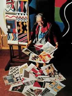 an older woman sitting in front of a pile of quilts and rugs on the floor