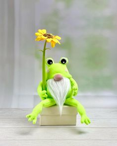 a green frog sitting on top of a wooden block next to a yellow sunflower