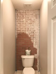 a white toilet sitting inside of a bathroom next to a brick wall and flooring