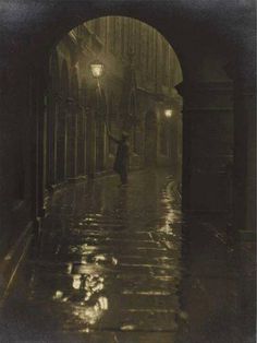 an old black and white photo of a person walking down the street in the rain