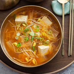 a bowl of soup with tofu, corn and green onions on a wooden plate