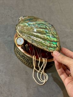 a hand holding a shell shaped box with pearls on the bottom and chain around it