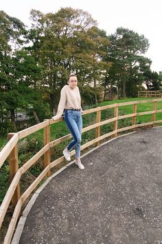 a woman standing on top of a wooden bridge next to a lush green field with trees