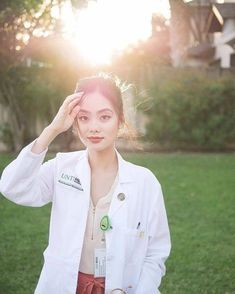 a woman in a white lab coat is standing on the grass with her hands behind her head