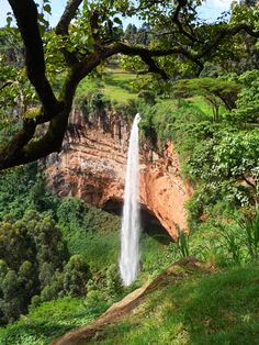 a large waterfall in the middle of a lush green valley with trees on both sides