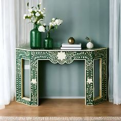 a green console table with white flowers and vases on top, against a blue wall