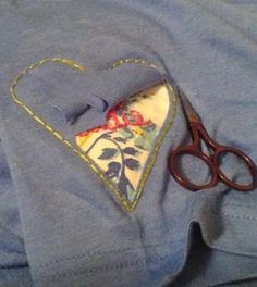 a pair of scissors sitting on top of a blue shirt with a heart shaped pocket