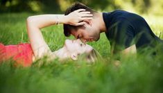 a man and woman are laying in the grass with their heads touching each other's foreheads