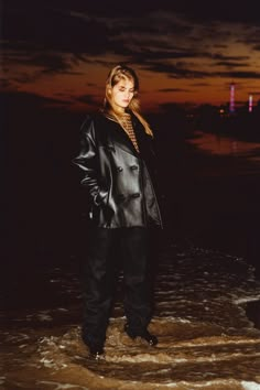 a woman is standing in the water at night wearing a black leather jacket and pants