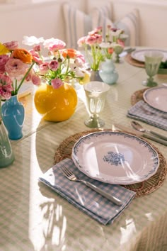 the table is set with plates and vases filled with colorful flowers in blue, yellow, pink and white