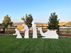 three sculptures in the shape of people and a baby jesus are on grass near trees