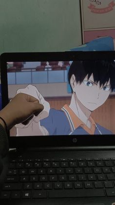 a person is playing on a laptop with an anime character in the screen behind them