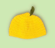 a crocheted yellow hat with a small green leaf on the top of it