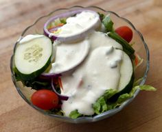 a salad with cucumbers, tomatoes and dressing in a glass bowl on a wooden table