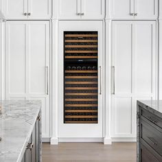 a wine cooler in the middle of a kitchen with marble counter tops and white cabinets