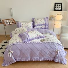 a bed with purple comforter and pillows in a room next to a white chair