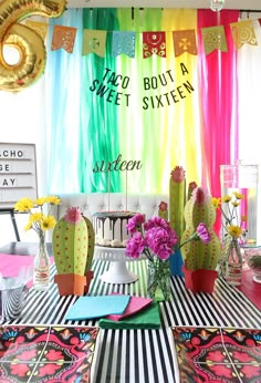 a table topped with vases filled with flowers next to a rainbow colored wall hanging from the ceiling