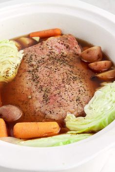 a white bowl filled with meat, carrots and cabbage next to some cut up veggies