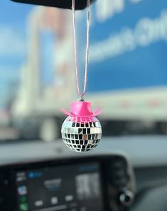 a disco ball ornament hanging from the dashboard of a car with a pink bow