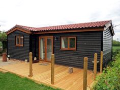 a small black cabin with wooden decking in the grass