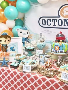 a table topped with lots of cakes and desserts next to balloons in the shape of animals