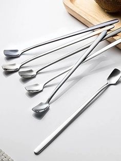 six spoons are lined up on a cutting board next to a loaf of bread