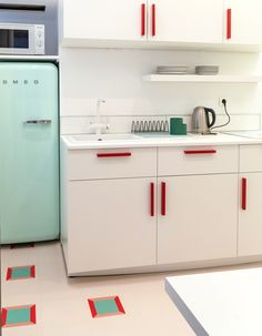 a kitchen with white cabinets and red trim on the countertops, along with a green refrigerator freezer