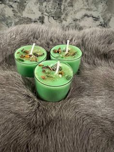 three green candles sitting on top of a furry surface