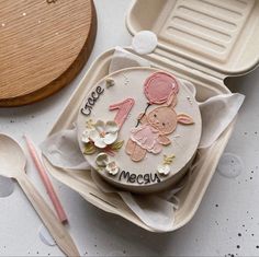 a decorated cake in a box with spoons and utensils next to it