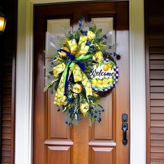 a welcome wreath on the front door of a house with yellow roses and greenery