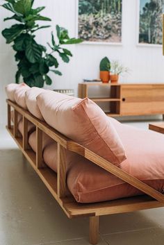 a wooden bench with pillows on it in front of a potted plant and other furniture