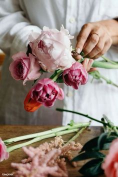 a person arranging flowers on a table with pink and white blooms in the foreground