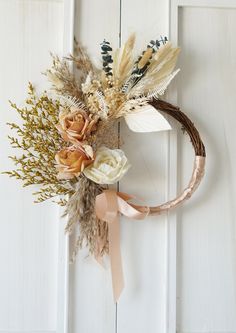 a wreath with dried flowers and feathers hanging on a white door handle, next to a pink ribbon