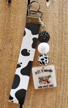 a cow print keychain hanging from a wooden door with two charms attached to it