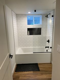 a bathroom with white tile and wood flooring is seen from the doorway to the bathtub