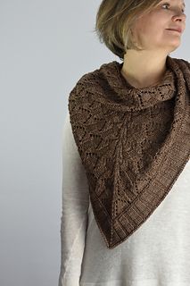 a woman wearing a brown knitted shawl and white shirt standing in front of a gray background