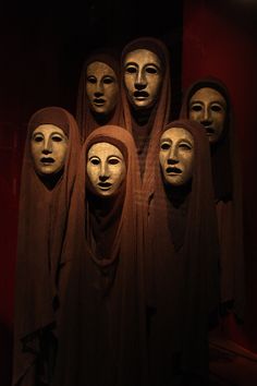 several masks are arranged in the shape of heads on display at an art museum,