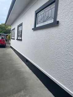 a red car parked in front of a white building with black trim on the side