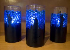 three vases with blue lights in them sitting on a wooden table next to each other