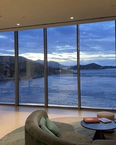 a living room filled with furniture and large windows looking out to the water at dusk