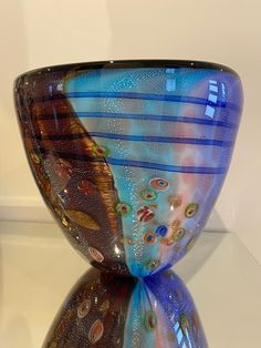 a colorful glass vase sitting on top of a white table next to a mirror wall