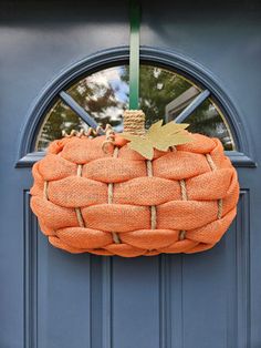 an orange burlocked pumpkin hanging on a blue front door with a green ribbon