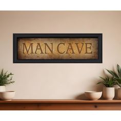 a man cave sign hanging on the wall next to potted plants and two white bowls