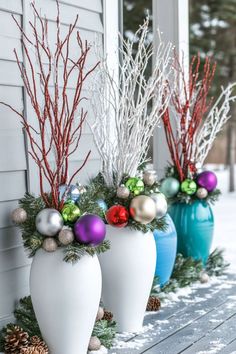 White and blue vases feature festive arrangements of colorful ornaments, pine branches, and red and white twigs, set on a snowy wooden porch. Christmas Decor Simple Ideas, Christmas Porch Planters Diy, Outdoor Xmas Planter Ideas, Cheap Christmas Porch Decor, Winter Wonderland Outside Decorations, Christmas Garden Decorations Outdoor, Diy Christmas Planter Ideas, Diy Outdoor Christmas Planter Ideas, Gnome Christmas Decor Ideas