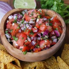 a wooden bowl filled with salsa surrounded by tortilla chips and cilantro